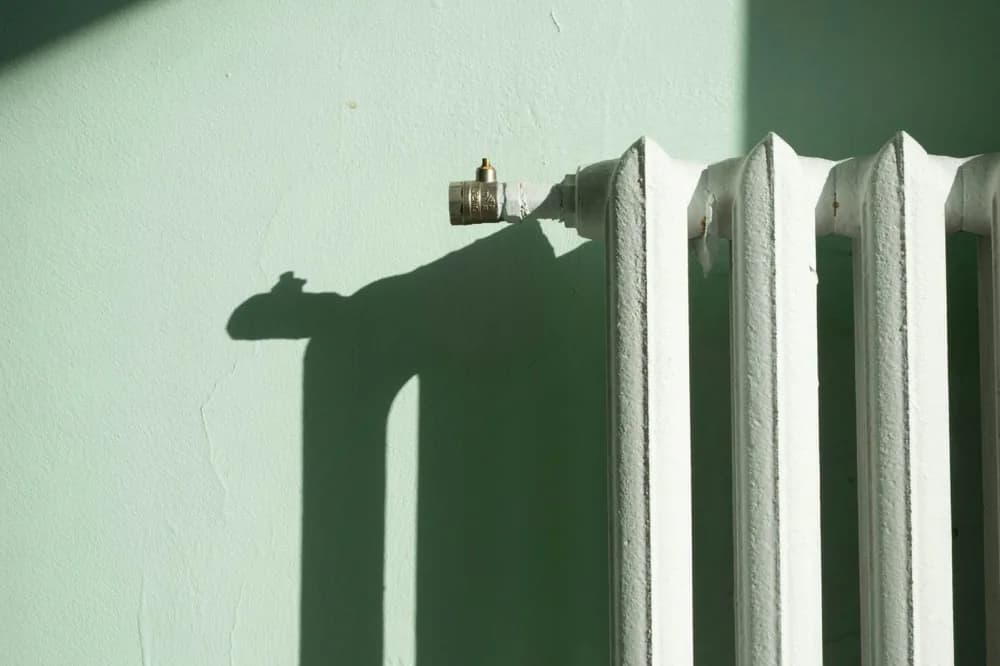Radiateur blanc contre un mur vert pâle, ombre portée nette