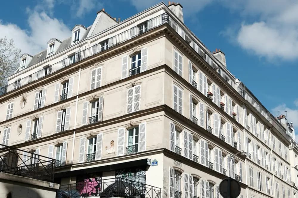 Immeuble ancien à l'angle de deux rues, volets clairs et toiture d'ardoise