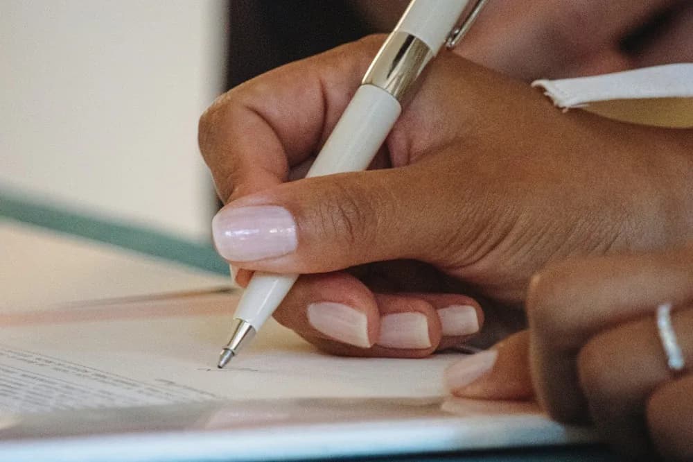 Main qui écrit au stylo sur une feuille posée à plat